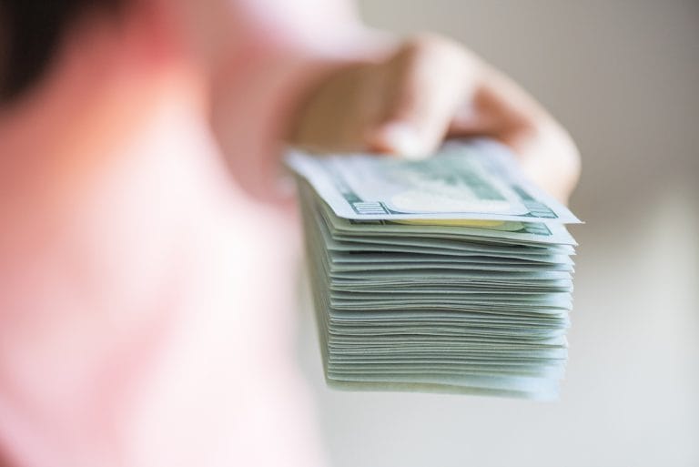 Cum să faci economii inteligente pentru pensie Soft focus on woman hands proposing money us dollar bills to you.